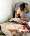 Afghan man bending over a hospital bed; in the foreground are bloodstained sheets covering dead people on two other beds.