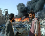 Two Afghan men watch the black smoke rising from a nearby burning building