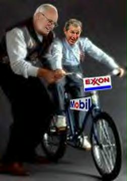 G.W., the size of  a little boy, is all excited as he learns to ride a bicycle, and he's being steadied and encouraged by Dick Cheney as his proud father. The bicycle has signs on it which read 'Exxon' and 'Mobil'.