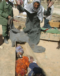 Photo of the same man holding his arms up as he looks down in anguish at the dead bodies of his children and baby.