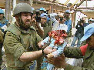 Photo shows a helmeted man in a green military uniform with no markings, and he is handing the body of a baby to a man wearing a light blue cap, as other men stare and newsmen take photos. There is no head on the baby's body. Where the baby's head was there is a mass of bloody, mangled flesh hanging down over his shoulders and chest. It is a very small baby with tiny arms and hands, probably less than a year old, the body dressed in little pale blue baby clothes. This is apparently in Qana, Lebanon, the site of a major atrocity committed by the Israeli military.