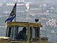 photo of a dirty yellow bulldozer cab with a dirt-stained Israeli flag mounted on it; inside is the silhouette of the driver