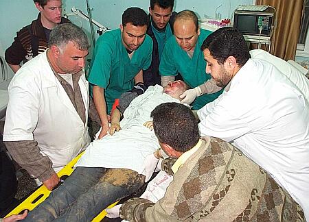 photo of Rachel Corrie's lifeless body on a stretcher in the hospital, surrounded by sad doctors and stretcher bearers. There is a patch of dirt on her jeans on her left thigh and her face is stained with dirt and blood.