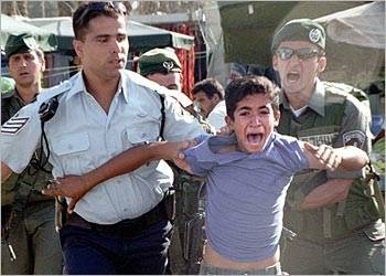 Photo shows an Israeli soldier and policeman manhandling a small Palestinian boy who looks around 10-12 years of age.  The boy is crying and screaming in fright, directly facing the viewer, about 7 to 10 feet away. Behind him the Israeli policeman is gripping the boy’s shirt tightly and marching him forward, and the Israeli pig has a very cruel, tight look on his ugly face as he clenches his teeth and looks down at the boy with cold hatred. Next to the Israeli pig is an Israeli soldier wearing sunglasses and a green beret, and his mouth is wide open in the midst of screaming some hateful thing at the crying boy. His hands are out of sight behind the boy, but the soldier’s aggressive stance - legs spread apart, torso leaning toward the boy, taut muscles in the visible portion of his forearm - suggests he is doing something aggressive, perhaps jabbing his gun in the boy’s back or shoving or hitting him.