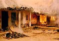 A dead body lying in front of a burning hut