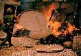A helmeted U.S. Army soldier tossing a large circular basket onto a burning pile of other baskets and debris.